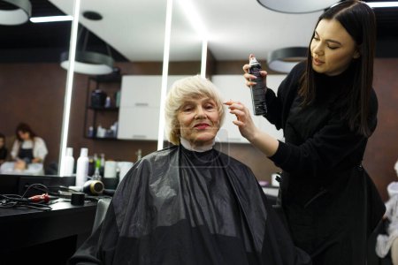 Téléchargez les photos : Portrait d'une femme âgée visitant un coiffeur professionnel. Un coiffeur expérimenté fait coiffure pour un client - en image libre de droit