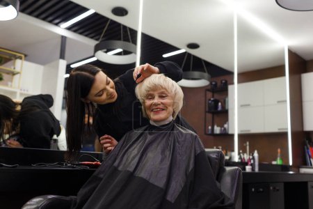 Photo for Portrait of an elderly woman visiting a professional hairdresser. An experienced hairdresser does hair styling for a client - Royalty Free Image