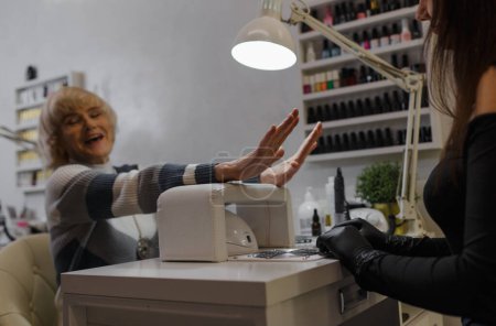 Téléchargez les photos : Une femme âgée sourit joyeusement, satisfaite de sa manucure dans un salon de beauté. - en image libre de droit