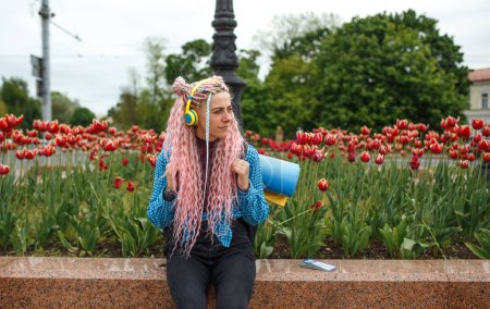 Téléchargez les photos : Une fille avec des écouteurs et des cheveux roses voyage autour de la ville avec un sac à dos sur les épaules. - en image libre de droit