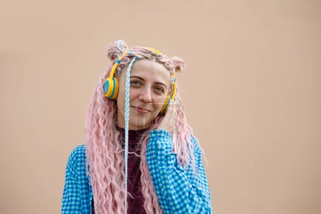 Téléchargez les photos : Une jeune femme heureuse aux cheveux longs roses et à la chemise bleue. Une fille avec un casque sur fond lumineux. Espace vide pour le texte publicitaire. - en image libre de droit