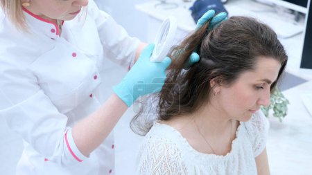 Foto de Un tricólogo examina la condición del cabello en la cabeza del paciente usando una lente. - Imagen libre de derechos