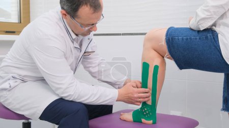 Téléchargez les photos : Le médecin examine l'articulation de la cheville malade du patient pour y déceler des fractures. Le concept de la maladie de la cheville, entorses. Taping - en image libre de droit
