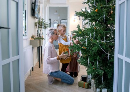 Téléchargez les photos : Famille, vacances d'hiver et le concept de personnes mère heureuse et petites filles décorer le sapin de Noël à la maison - en image libre de droit