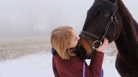 Téléchargez les photos : Une fille heureuse embrasse son cheval bien-aimé dans un champ pendant le brouillard. - en image libre de droit