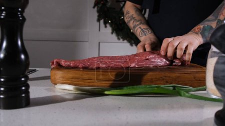Foto de El cocinero corta carne de res con un cuchillo en una tabla de cortar. El chef separa la entrecota de un trozo de carne fresca. - Imagen libre de derechos