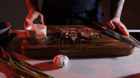 Photo for Pieces of cooked and sliced meat sprinkled with fresh onions lie on a wooden board in front of the cook ready to serve - Royalty Free Image