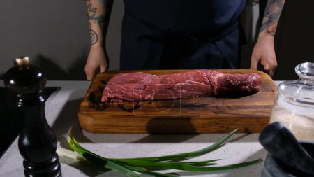 Foto de Un trozo de carne cruda se encuentra en la tabla de cortar delante del cocinero en la cocina - Imagen libre de derechos
