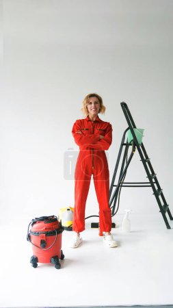 Téléchargez les photos : Une fille en combinaison rouge vif d'une entreprise de nettoyage sur fond de fournitures de nettoyage - en image libre de droit