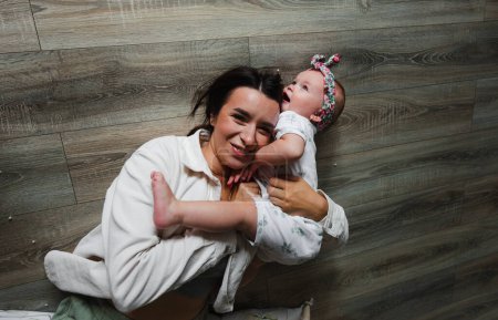 Photo for Portrait of a happy young mother and her little daughter hugging lying on the floor. - Royalty Free Image