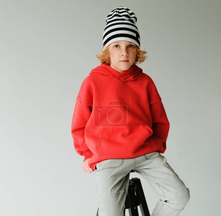 Foto de Un chico vestido de rojo impactante se sienta con confianza sobre un fondo gris. - Imagen libre de derechos