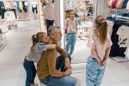 Photo for Father chooses clothes with young daughters in a fashion boutique - Royalty Free Image