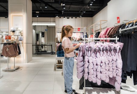 Une jeune fille parcourt des vêtements dans un magasin de vêtements, examinant différents styles et couleurs.
