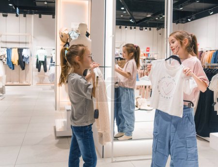 Deux jeunes filles, debout dans un magasin de vêtements, naviguent à travers les vêtements exposés avec un vif intérêt.