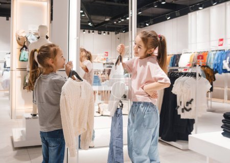 Deux filles, jeunes, naviguent dans les vêtements exposés dans un magasin de vêtements.