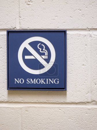 Photo for Blue "No Smoking" sign on a white cement cinderblock wall with a crossed out cigarette - Royalty Free Image