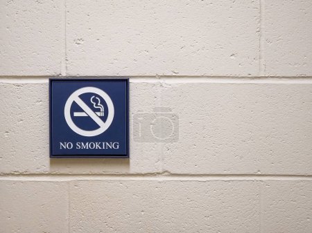 Photo for Blue "No Smoking" sign on a white cement cinderblock wall with a crossed out cigarette - Royalty Free Image