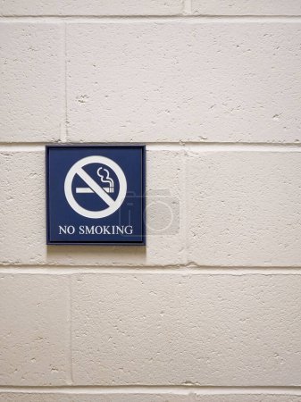 Photo for Vertical image of a blue "No Smoking" sign on a white cement cinderblock wall with a crossed out cigarette - Royalty Free Image