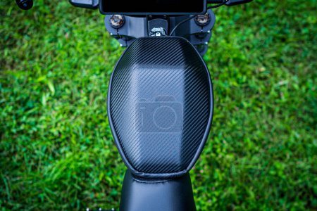 Téléchargez les photos : Un vélo électrique noir élégant, rappelant un cyclomoteur, se tient gracieusement dans un paysage herbeux serein, entouré d'arbres - en image libre de droit