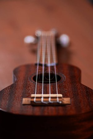 Photo for A charming ukulele gracing a wooden table, inviting musical moments with its acoustic allure and strings that resonate with a touch of Hawaiian serenity - Royalty Free Image