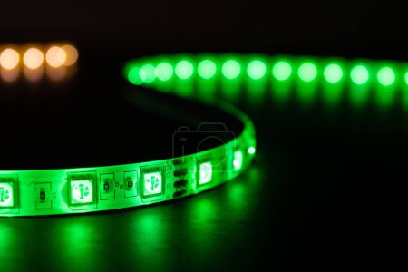 Photo for Bobbin with roll of glowing LED strip lighting placed on table, green and warm white color - Royalty Free Image