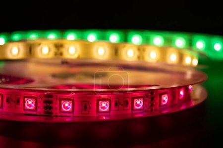 Photo for Bobbin with roll of glowing LED strip lighting placed on table, pink, green and warm white color - Royalty Free Image
