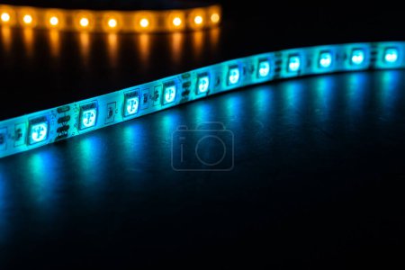 Photo for Bobbin with roll of glowing LED strip lighting placed on table, pink, and warm white,blue color in dark room - Royalty Free Image