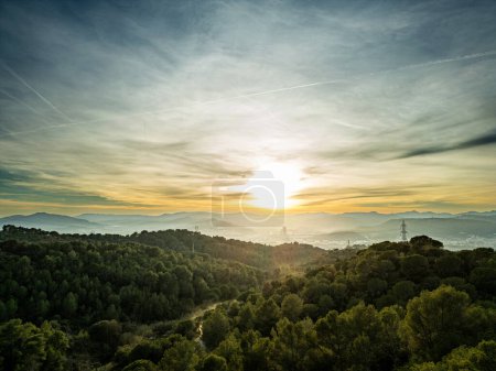Photo for Picturesque view of green trees in forest and mountains under cloudy sky with bright sun shining through clouds in evening time - Royalty Free Image
