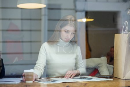 Photo for Beautiful woman reading magazine in cafe - Royalty Free Image