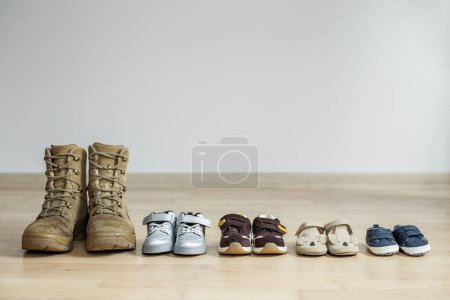 Foto de Botas militares viejas y muchos zapatos de bebé en el piso de madera. Concepto de padre militar y familia. Copiar espacio - Imagen libre de derechos