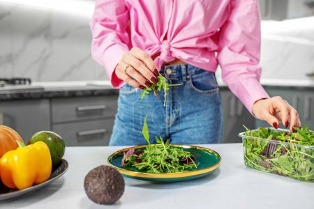 Photo for Woman is preparing salad from vegetables and spring mix in kitchen. Concept of healthy food, diet and eco products - Royalty Free Image