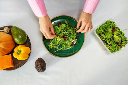 Photo for Woman is preparing salad from vegetables and spring mix in kitchen. Concept of healthy food, diet and eco products - Royalty Free Image