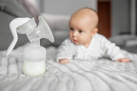 Téléchargez les photos : Child care concept. Breast pump with milk on background of small cute baby. Selective focus, copy space. - en image libre de droit