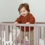 Cute laughing baby standing in round bed. Little girl learns to stand in her crib.