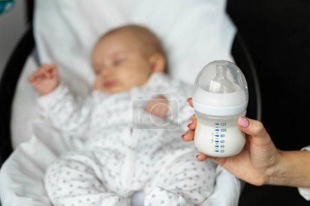 Concepto de cuidado infantil. El biberón de la comida para bebés en las manos de la madre sobre el fondo del bebé pequeño.
