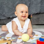Baby creep on floor of nursery grabbing colorful ball. Colorful toys. Baby development. Sensory experience