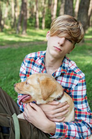 Teenage boy hugs labrador dog in park in summer. Friendship and pets concept. Gen Z.