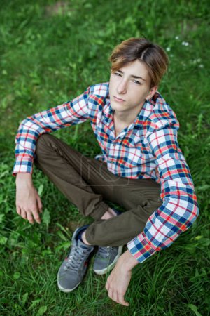 Téléchargez les photos : Portrait d'un adolescent sérieux assis sur l'herbe dans le parc. Gén Z. ! Vue de dessus. Développement de l'identité - en image libre de droit