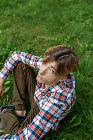Portrait of serious teenager sitting on grass in park. Gen Z. Top view. Identity development