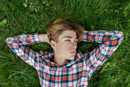 Foto de Retrato de un adolescente serio que yace en la hierba y descansa. Gen Z. Desarrollo de la identidad. - Imagen libre de derechos