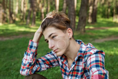 Téléchargez les photos : Portrait d'un adolescent sérieux assis sur l'herbe dans le parc. Gén Z. ! Développement de l'identité. - en image libre de droit