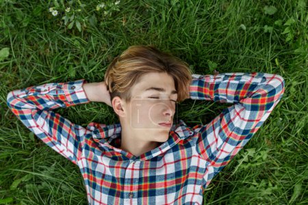 Foto de Retrato de un adolescente serio que yace en la hierba y descansa. Gen Z. Desarrollo de la identidad. Dormir.. - Imagen libre de derechos