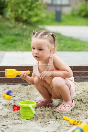 Little girl playing in sandbox at playground outdoors. Toddler playing with sand molds and making mudpies. Outdoor creative activities for kids.