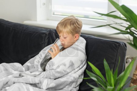 Kranker preteen Junge mit hohem Fieber und Halsschmerzen und einem schlechten Gefühl, zu Hause auf dem Sofa sitzend