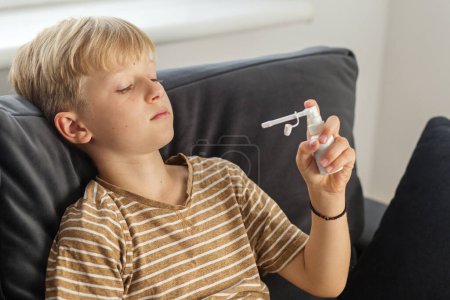 Frío estacional. Spray para la garganta. Niño preadolescente enfermo que usa aerosol oral para recuperarse del dolor de garganta.