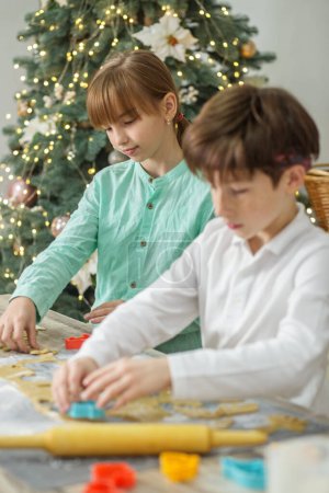 Foto de Dos niños preparan galletas de jengibre para las vacaciones de Navidad y juegan con cortadores de galletas. - Imagen libre de derechos