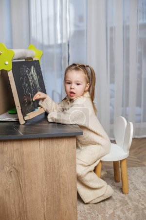 Photo for Early brain development. Toddler girl draws on blackboard at home. - Royalty Free Image