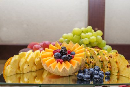 Téléchargez les photos : Manger à l'événement. Une exposition traiteur attrayante d'ananas sculptés, cantaloup, raisins et baies mélangées sur plateau en verre réfléchissant. - en image libre de droit