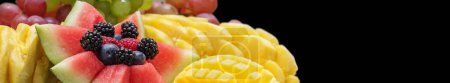Téléchargez les photos : Gros plan panoramique de l'affichage dynamique des fruits avec pastèque, ananas, baies et tranches de mangue sur fond sombre. - en image libre de droit