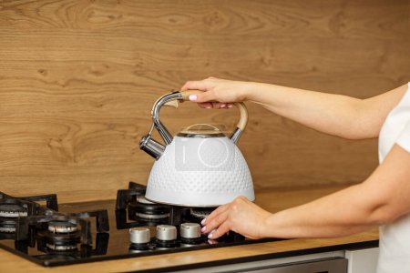 Person's hand is placing stylish white kettle on stove top, preparing for hot beverage in cozy kitchen atmosphere.